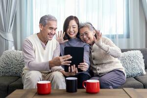 Aziatisch familie bijeenkomst van senior vader moeder en dochter zittend Aan bankstel met gelukkig glimlach in pensioen huis terwijl hebben video telefoontje naar de andere relatie en neef lid foto