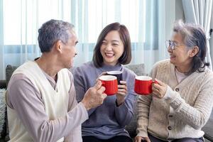 Aziatisch familie van senior vader moeder en dochter zittend Aan bankstel met gelukkig glimlach in pensioen huis drinken heet thee naar vieren hun vakantie samen voor ouderling zorg en uitgeven waardevol tijd foto