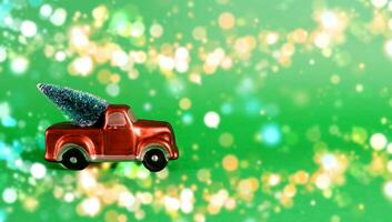 nieuw jaar kaart met plaats voor tekst. rood auto met een Kerstmis boom in de terug van een oppakken vrachtauto Aan een groen achtergrond met wazig bokeh foto