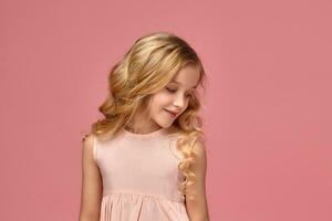 weinig meisje met een blond gekruld haar, in een roze jurk is poseren voor de camera foto