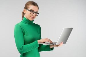 vrouw in halve draai werkt staand op een laptop. naar de camera kijken foto