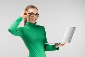 vrolijke vrouw met een bril werkt op een laptop die hem in haar handen houdt terwijl ze tegen de witte achtergrond staat. kijkt naar de camera foto