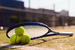 drie tennisballen en racket op hardcourt onder zonlicht foto