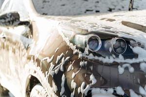 close-up van de zwarte auto gewassen door hoge druk van water en zeep bij carwash. schoonmaak dienstverleningsconcept. zelfbediening autowasstation foto
