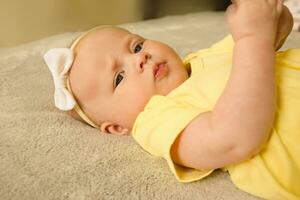 schattig, zoet en charmant weinig meisje in een geel bodysuit aan het liegen Aan de bed en lachend. foto