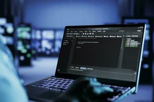 gecertificeerd technicus rennen code en programmering Aan laptop, probleemoplossen en upgraden hoog tech faciliteit ontworpen naar accommoderen meerdere rijen van ten volle operationeel server installaties, dichtbij omhoog foto