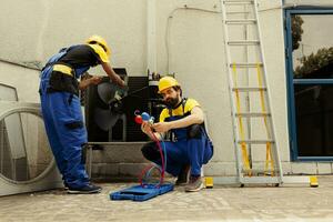 ingenieur Verwijderen aarde en stof van lucht conditioner verdamper en condensor wikkelen terwijl collega toepassingen verdeelstuk meters naar controleren voor koelmiddel lekken en lezen druk in hvac systeem foto