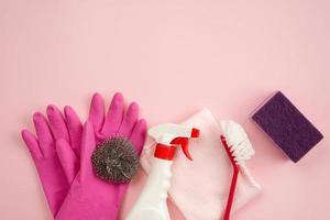 huishoudborstel, keukenspons, reinigingsspray en vod liggend op roze achtergrond foto