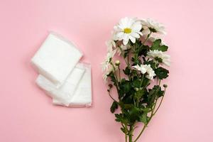 vrouwelijke pakking voor menstruatie en witte bloem op een roze achtergrond.