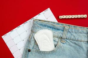 het volgen van de menstruatiecyclus en ovulatie. op een rode achtergrond vrouwen pads in jeans zak. foto