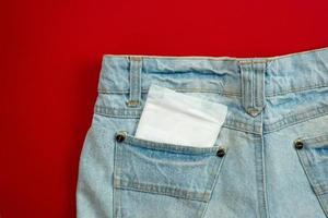 vrouwenstootkussen in de zak van vrouwelijke jeans op een rode achtergrond. - afbeelding foto