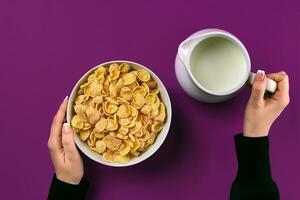 voedsel en mensen concept - handen van vrouw aan het eten granen maïs vlokken voor ontbijt en gieten melk foto