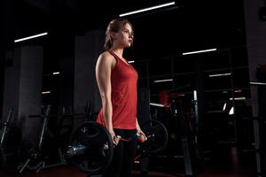 jong mooi vrouw aan het doen oefening met bar in een Sportschool. atletisch meisje aan het doen training in een geschiktheid centrum. foto