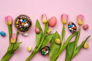veelkleurig snoep in de chocolade-eieren en verse tulpen liggen op een roze tafel. - paasconcept foto