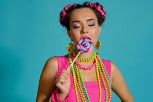 lief meisje met een veelkleurig vlechtjes kapsel en helder verzinnen, poseren in studio tegen een blauw achtergrond, Holding een lolly in haar hand. foto