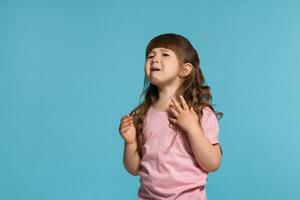 mooi weinig meisje vervelend in een roze t-shirt is poseren tegen een blauw studio achtergrond. foto