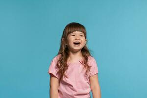 mooi weinig meisje vervelend in een roze t-shirt is poseren tegen een blauw studio achtergrond. foto