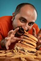detailopname portret van een middelbare leeftijd Mens met baard, gekleed in een rood coltrui, poseren met hamburgers en Frans Patat. blauw achtergrond. snel voedsel. foto