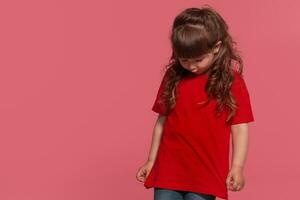 detailopname portret van een weinig brunette meisje gekleed in een rood t-shirt poseren tegen een roze studio achtergrond. oprecht emoties concept. foto