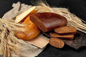 gesneden broden van wit en rogge brood met jute en oren van tarwe Aan zwart achtergrond foto