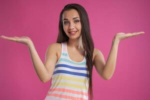 brunette vrouw met lang haar, gekleed in kleurrijk gestreept shirt, poseren tegen roze studio achtergrond. oprecht emoties. detailopname. foto