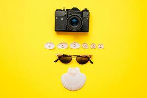 zonnebril, een vintage camera en schelpen liggen op een gele achtergrond. vrije tijd concept