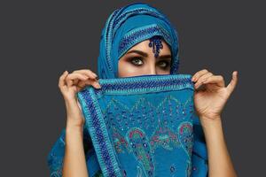 studio schot van een jong mooi vrouw vervelend de blauw hijab versierd met pailletten en sieraden. Arabisch stijl. foto