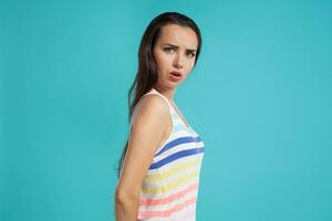 brunette vrouw met lang haar, gekleed in kleurrijk gestreept shirt, poseren tegen blauw studio achtergrond. oprecht emoties. detailopname. foto