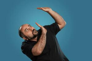 detailopname portret van een brunet middelbare leeftijd Mens met baard, gekleed in een zwart t-shirt en poseren tegen een blauw achtergrond. foto