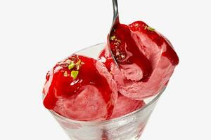 scheppen van fruit ijs room bekroond met BES jam en pistache kruimels in glas kom met lepel foto