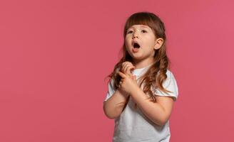 detailopname portret van een weinig brunette meisje gekleed in een wit t-shirt poseren tegen een roze studio achtergrond. oprecht emoties concept. foto