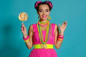 lief meisje met een veelkleurig vlechtjes kapsel en helder verzinnen, poseren in studio tegen een blauw achtergrond, Holding een lolly in haar hand. foto