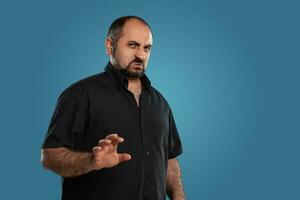 detailopname portret van een brunet middelbare leeftijd Mens met baard, gekleed in een zwart t-shirt en poseren tegen een blauw achtergrond. foto