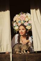 brunette meisje in een wit oekraïens authentiek nationaal kostuum en een krans van bloemen is is op zoek uit van de venster. detailopname. foto