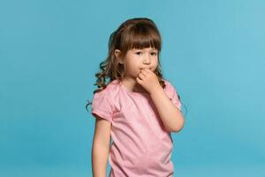mooi weinig meisje vervelend in een roze t-shirt is poseren tegen een blauw studio achtergrond. foto