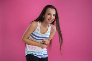 brunette vrouw met lang haar, gekleed in kleurrijk gestreept shirt, poseren tegen roze studio achtergrond. oprecht emoties. detailopname. foto