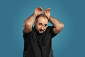 detailopname portret van een brunet middelbare leeftijd Mens met baard, gekleed in een zwart t-shirt en poseren tegen een blauw achtergrond. foto