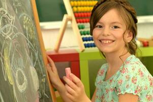 zoet weinig meisje aan het leren gelukkig in voorkant van haar schoolbord foto