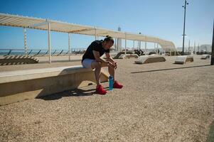 midden- oud uitgeput sportman zittend Aan de steen bank Aan de promenade, resting na zwaar training buitenshuis foto