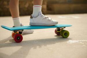 staand Aan skateboard Aan een been. dichtbij omhoog visie van een weinig kind meisje poten in blauw schoenen. foto