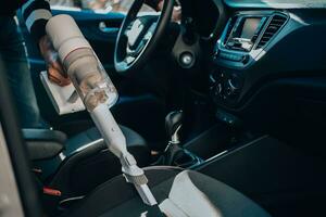 detailopname van een Mens stofzuigen een auto stoel. de hand- houdt een draadloos vacuüm schoonmaakster en reinigt de interieur van de auto. foto