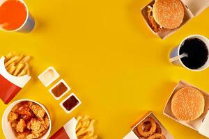 snel voedsel schotel top visie. vlees hamburger, aardappel chips en wiggen. nemen weg samenstelling. Frans Patat, Hamburger, mayonaise en ketchup sauzen Aan geel achtergrond. foto