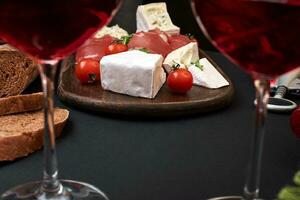 prosciutto, salami, baguette plakjes, tomaten en gek rustiek houten bord, twee bril van rood wijn over- zwart achtergrond foto