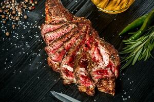 barbecue droog oud rib van rundvlees met kruid, groenten en een glas van licht bier detailopname Aan zwart houten achtergrond foto