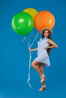 volledige lengte schot van glimlachen jong vrouw op zoek camera en Holding kleurrijk lucht ballonnen geïsoleerd over- blauw foto