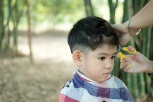 kapper snijdend haar- van een Aziatisch jongen in een Open ruimte gevulde met bomen. foto