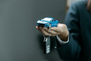 bedrijf hand- Holding blauw auto speelgoed. auto verzekering, garantie, verhuur, financieel, nieuw en reparatie concept. foto