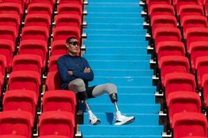 gehandicapt atleten in een blauw overhemd zittend Aan de rood stoelen Bij de stadion, bereiden voor rennen opleiding. foto
