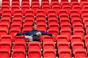 gehandicapt atleten in een blauw overhemd zittend Aan de rood stoelen Bij de stadion, bereiden voor rennen opleiding. foto