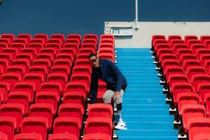 gehandicapt atleten in een blauw overhemd zittend Aan de rood stoelen Bij de stadion, bereiden voor rennen opleiding. foto